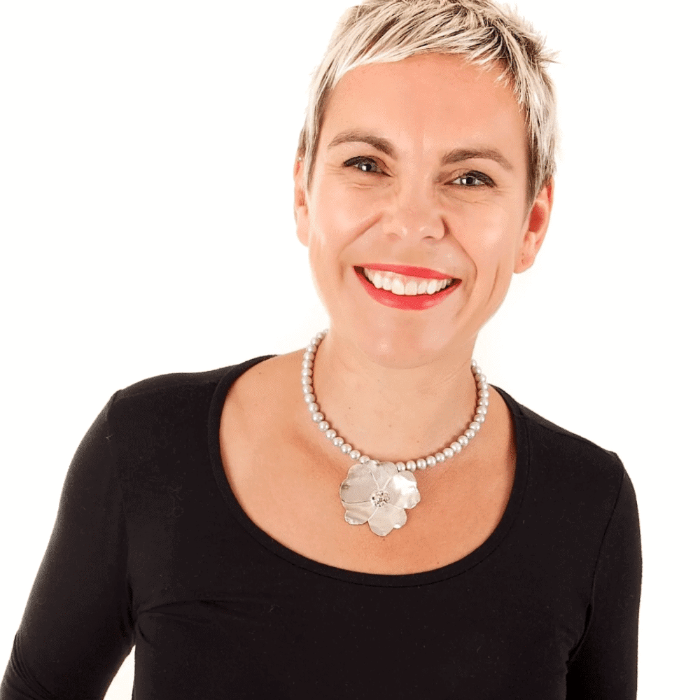 Confident woman with short hair smiling, wearing a black top and pearl necklace.