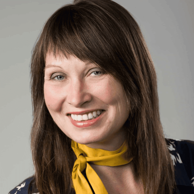 Smiling woman with brown hair wearing a yellow scarf, looking friendly and approachable.