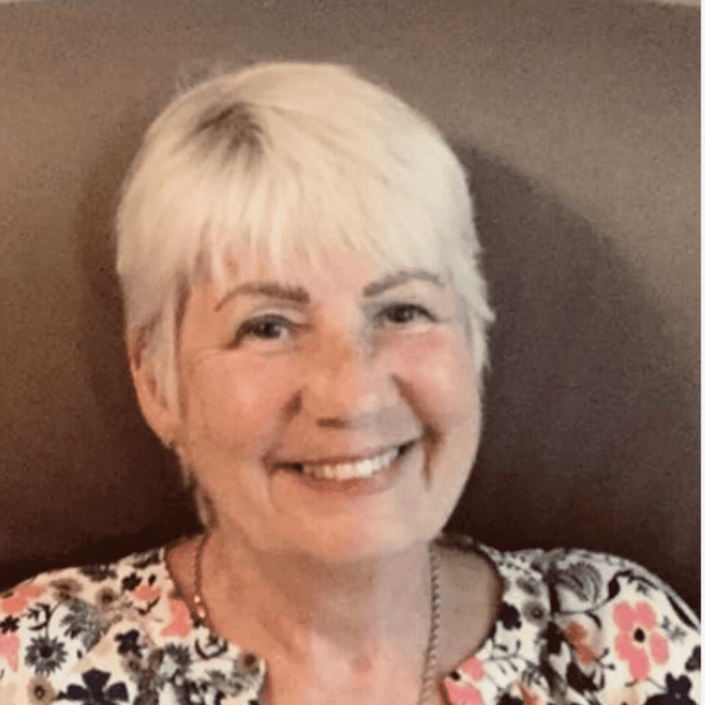 Smiling woman with short white hair and floral top at Raw Horizons.