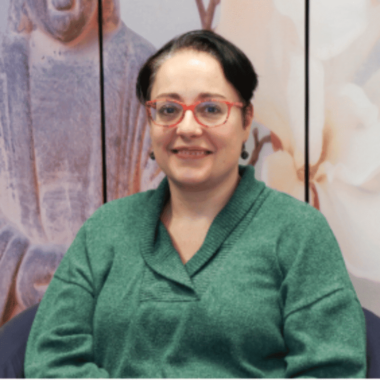Woman smiling in green sweater at Raw Horizons event, standing in front of artistic background.