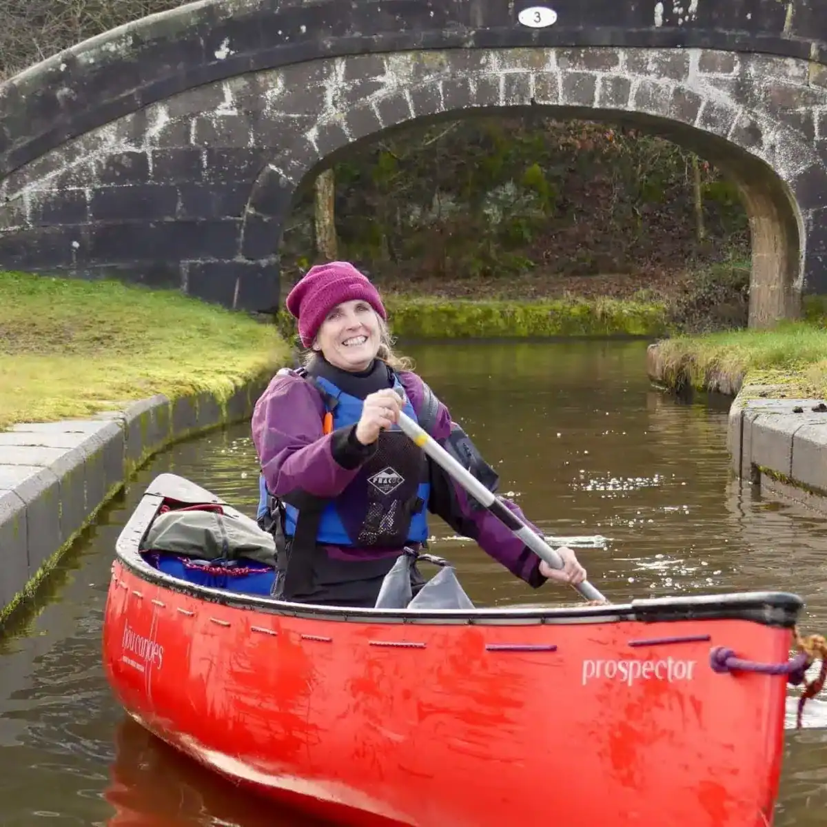 Kayaking on a peaceful canal near a stone bridge in a lush green setting.