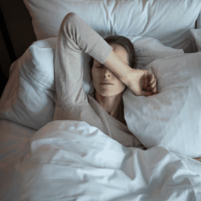 Woman resting peacefully in bed with eyes closed, relaxing in a cozy bedroom setting.