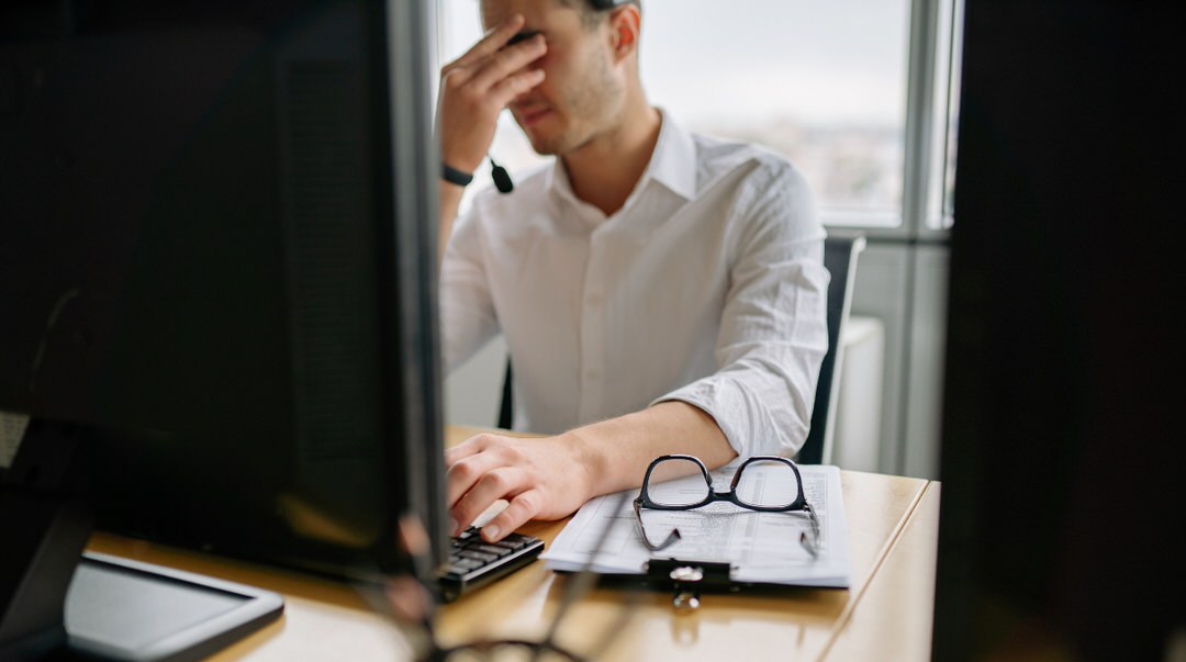 Frustrated man with glasses at desk, experiencing website issues.