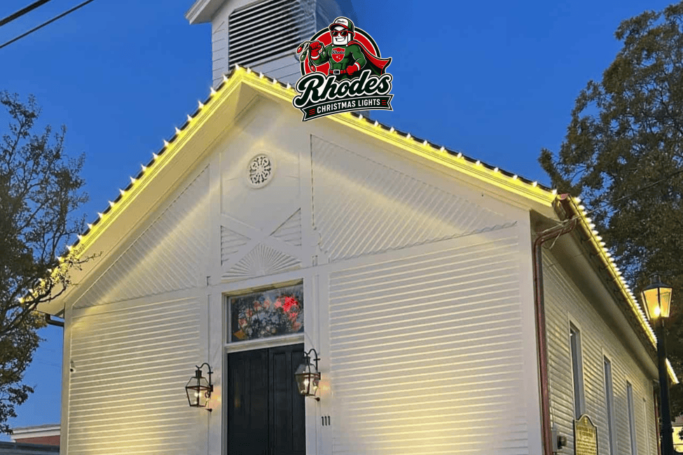 House decorated with yellow Christmas lights and Rhodes Christmas Lights logo at dusk.