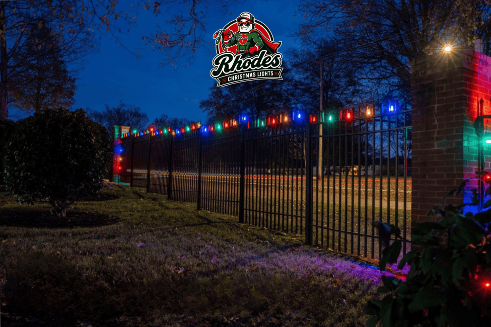 Colorful Christmas lights decorating a black metal fence at night.
