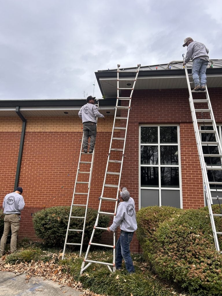 Workers installing Christmas lights on a building's roof during daytime.