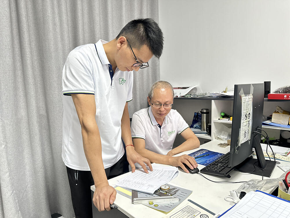 RIXI staff reviewing technical paperwork and components at an engineering workstation