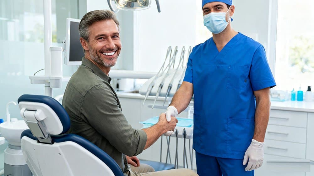 A happy patient thanks their dentist next to a comfortable premium dental chair, illustrating how it improves patient retention.