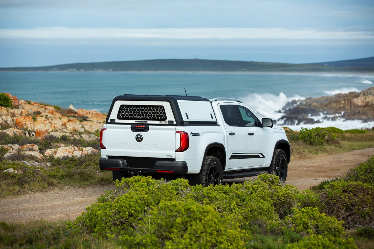 Stainless steel canopy on white pickup truck parked near rocky coastline with ocean view, showcasing durable and stylish vehicular canopy design.