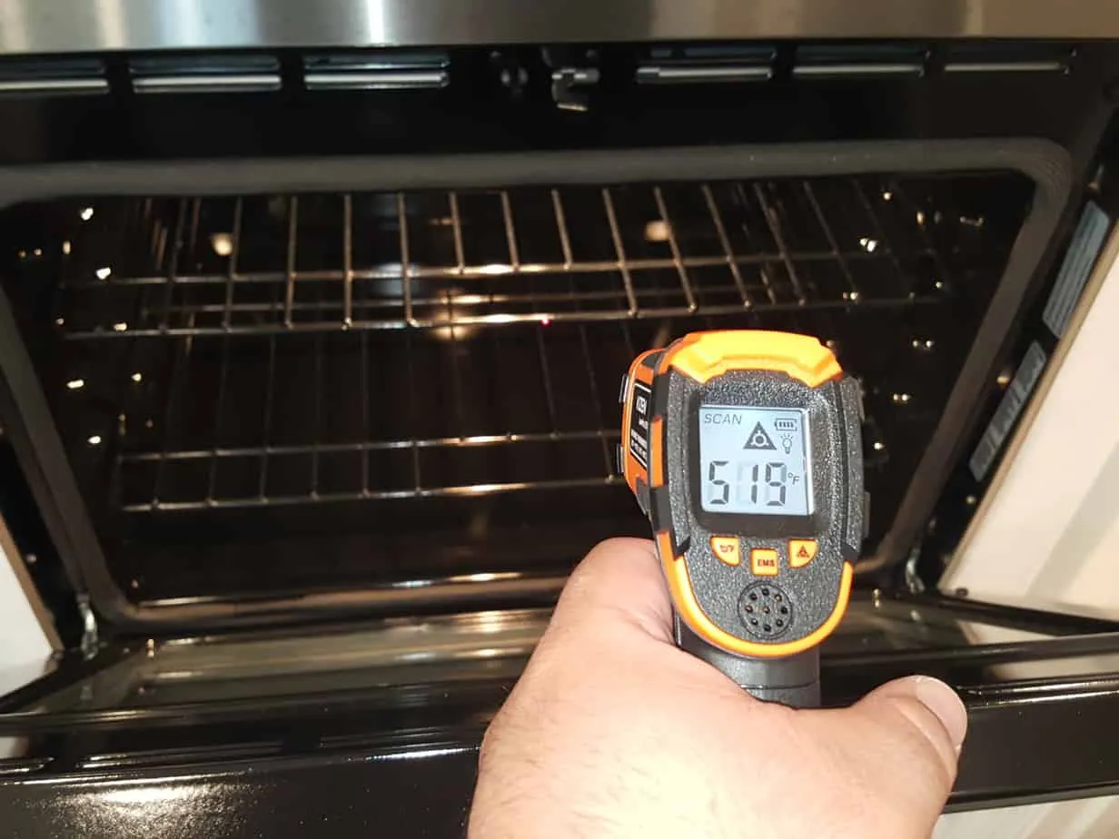 An inspector holding an infrared thermometer inside an open oven to read its temperature