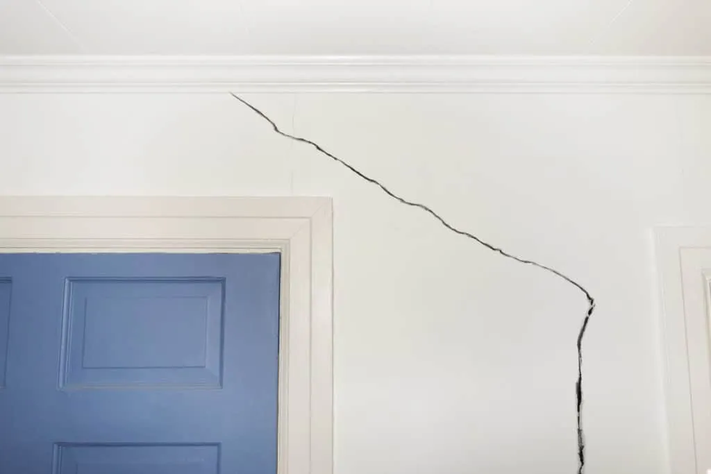 A stair-step crack running from a door frame to the ceiling in a painted interior wall