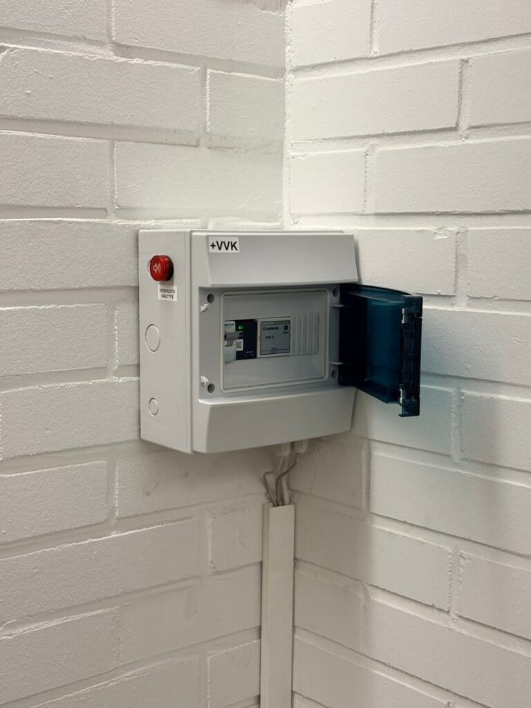 Sähkökeskus seinällä, valkoinen ja kiinnitetty valkoiseen tiiliseinään.