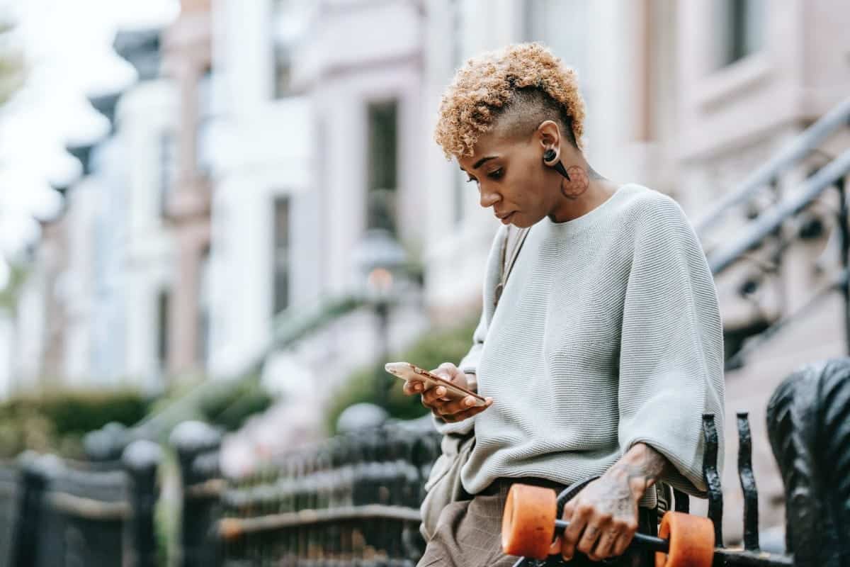 attentive ethnic woman chatting on smartphone in town
