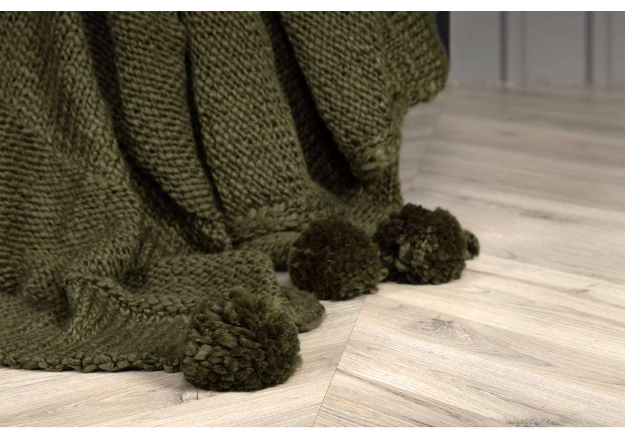 15943-204__004 Mörkgrön stickad filt och små pompom-tyg på en ljus träsoffa.