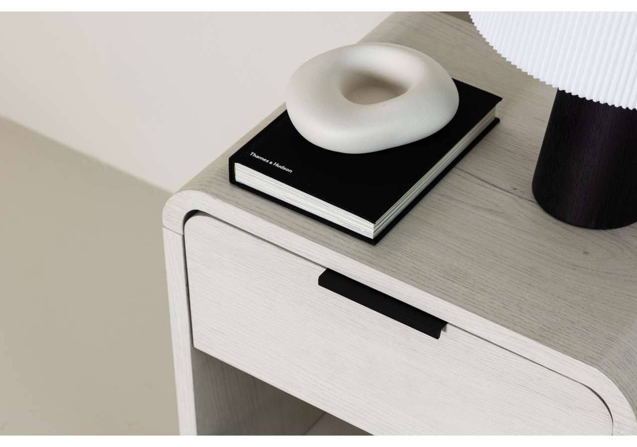 Elegant nightstand with black drawer handle and decorative items on top.