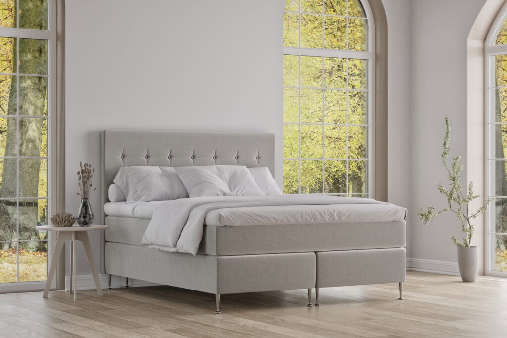 Elegant säng från Sängfabriken i modern design med vita textilier och stora fönster.