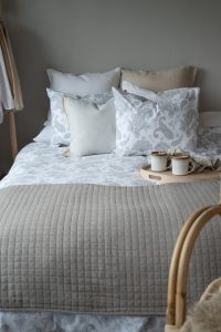 Fina sängkläder och kuddar i vitt och beige, mysig sovrumsmiljö med naturnära inredning.