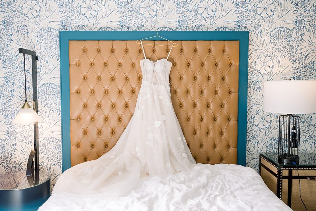 a wedding dress hanging on a hotel bed frame