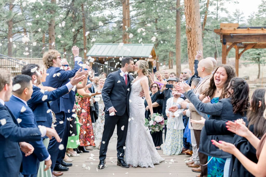 Bride and Groom share a kiss while everyone throws white rose petals
