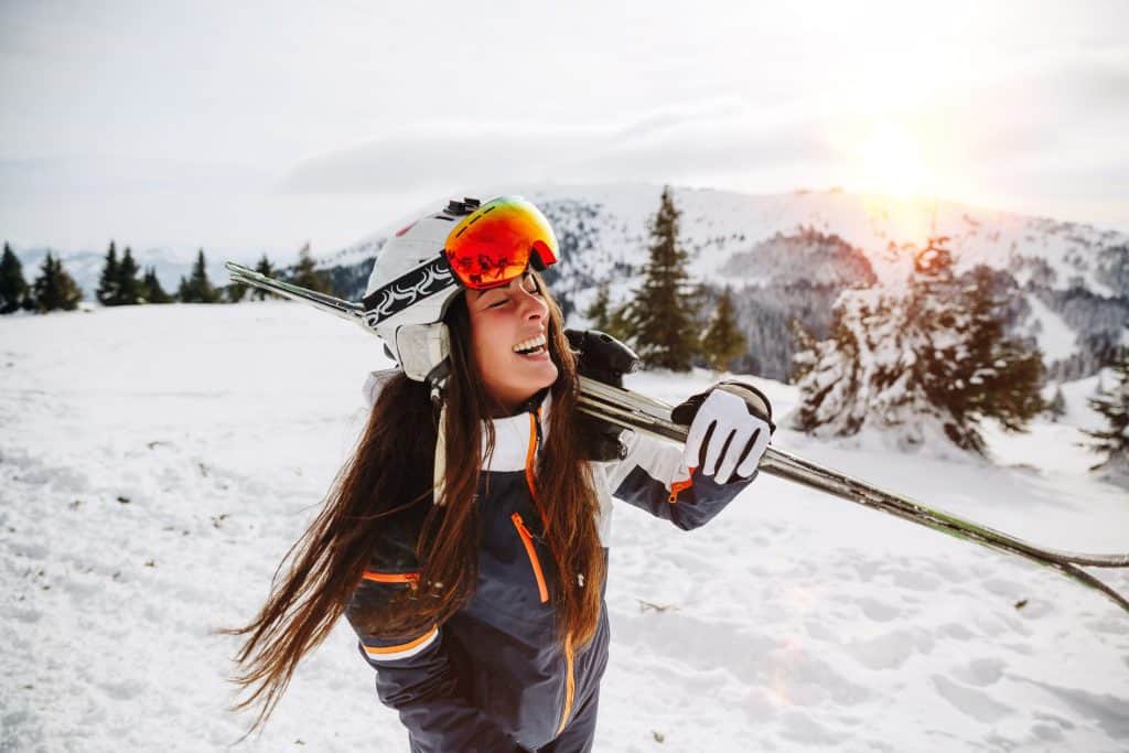 A happy woman standing in snowy mountains holding her snow skis
