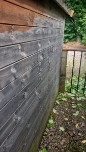 Weathered wooden shed exterior with grey stain, highlighting quality outdoor decorating services.
