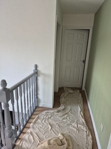 Smooth white and green interior wall painting by S Bond Decorating, with protective cloth on carpet.