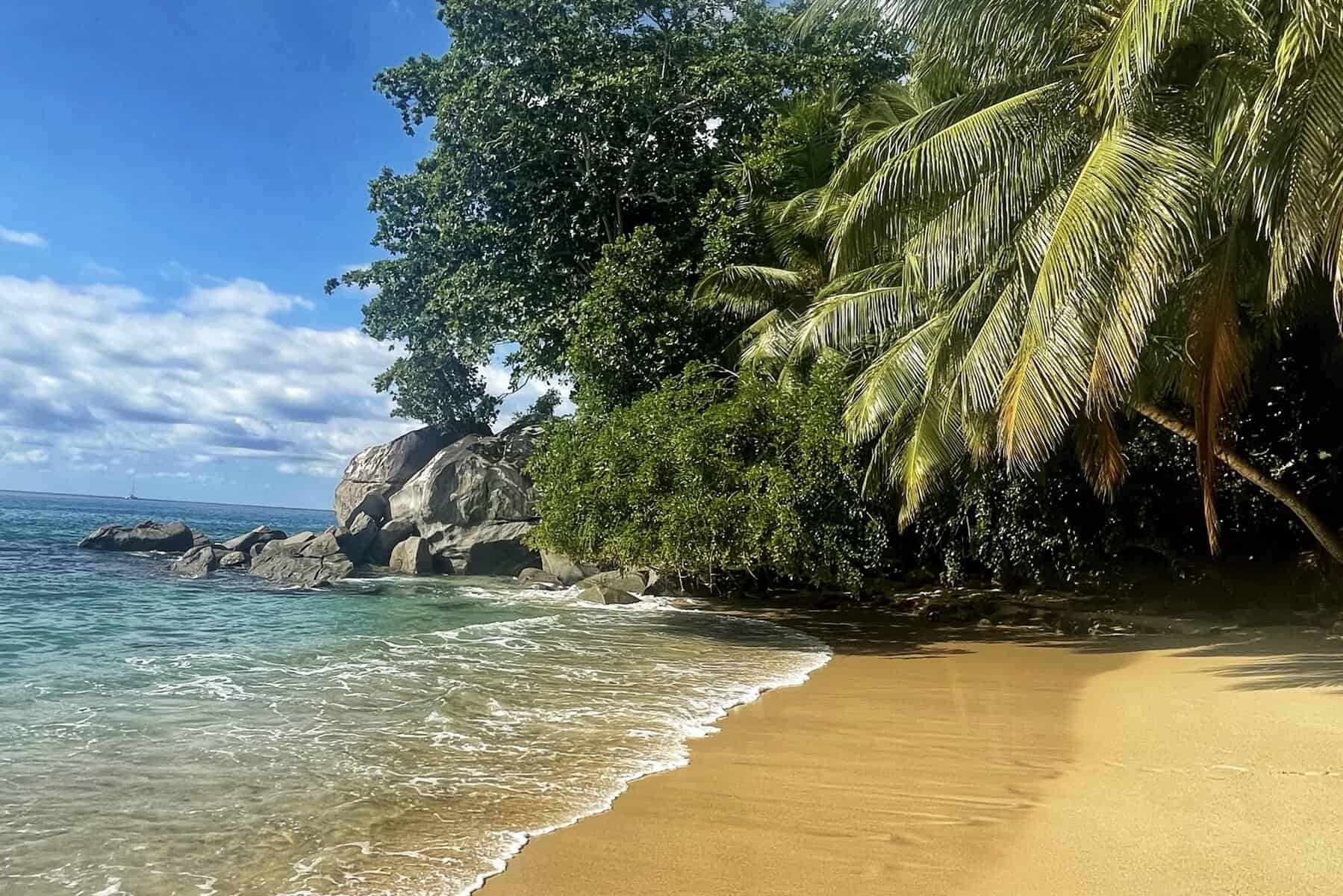 Sunset Beach Mahé Seychelles 2 Plage isolée avec sable doré, eaux turquoise et palmiers luxuriants, offrant un cadre paisible et naturel sur l'île de Mahé, Seychelles.
