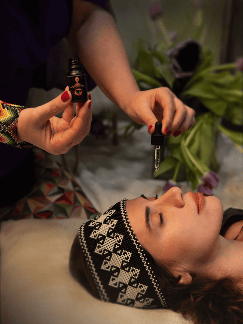 Vielka Flores holding essential oil and dropper over woman receiving holistic healing treatment at Shaman Hape Circle wellness center, promoting alternative healing methods.