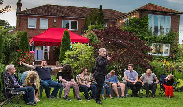 Outdoor gathering with speaker, people sitting in garden.