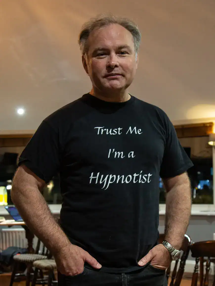 Person wearing 'Trust Me I'm a Hypnotist' shirt.