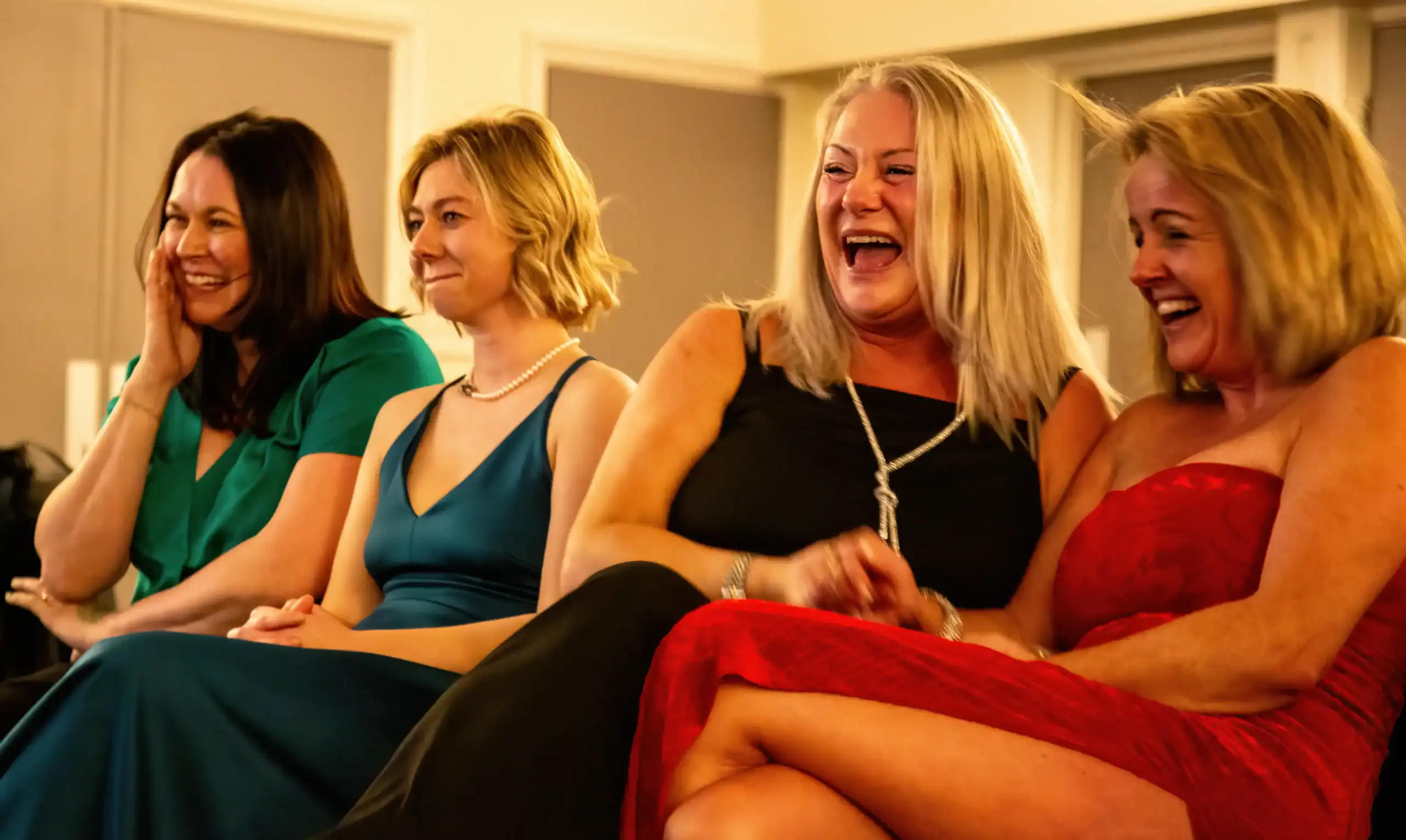 Four women laughing in colorful dresses at an event.