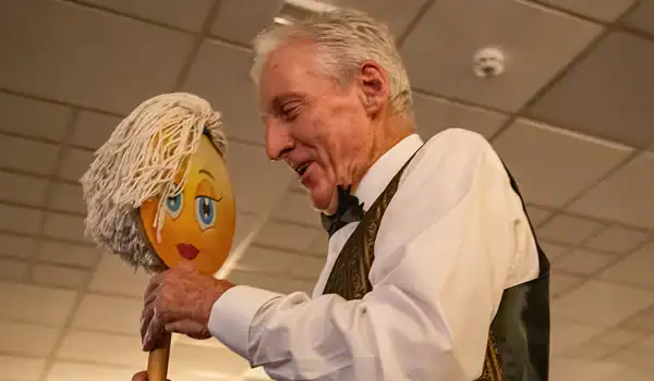 Man smiling at a funny face mop stick.