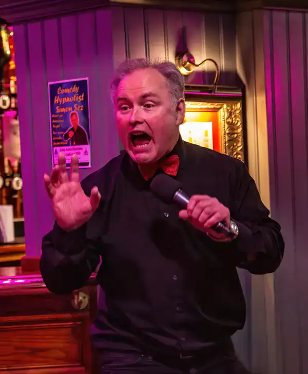 Comedian performing live, holding microphone, expressive face.