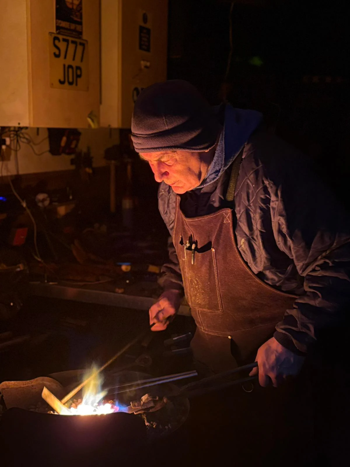 Blacksmith forging metal in workshop at night.
