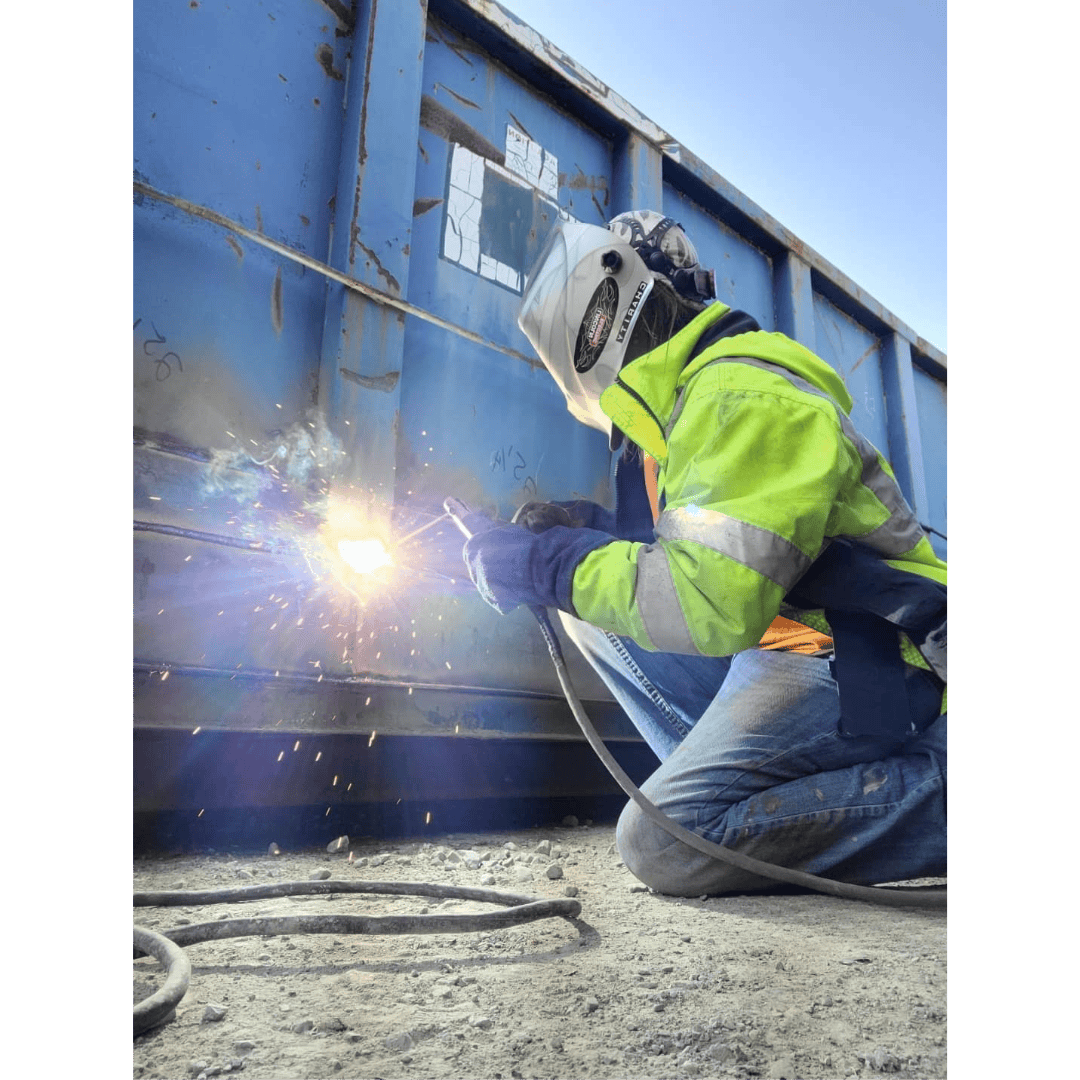 Welding worker in safety gear welding on a blue shipping container.