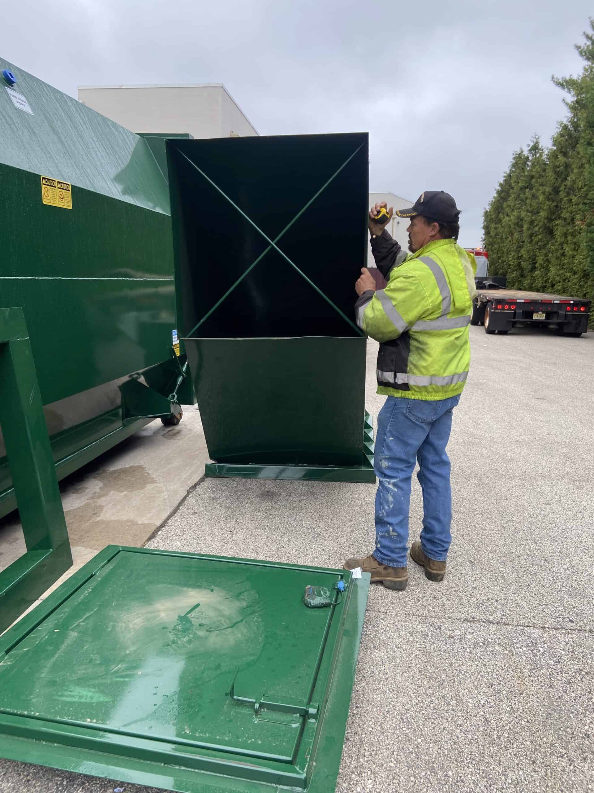 Portable waste container being assembled by a worker in safety gear.
