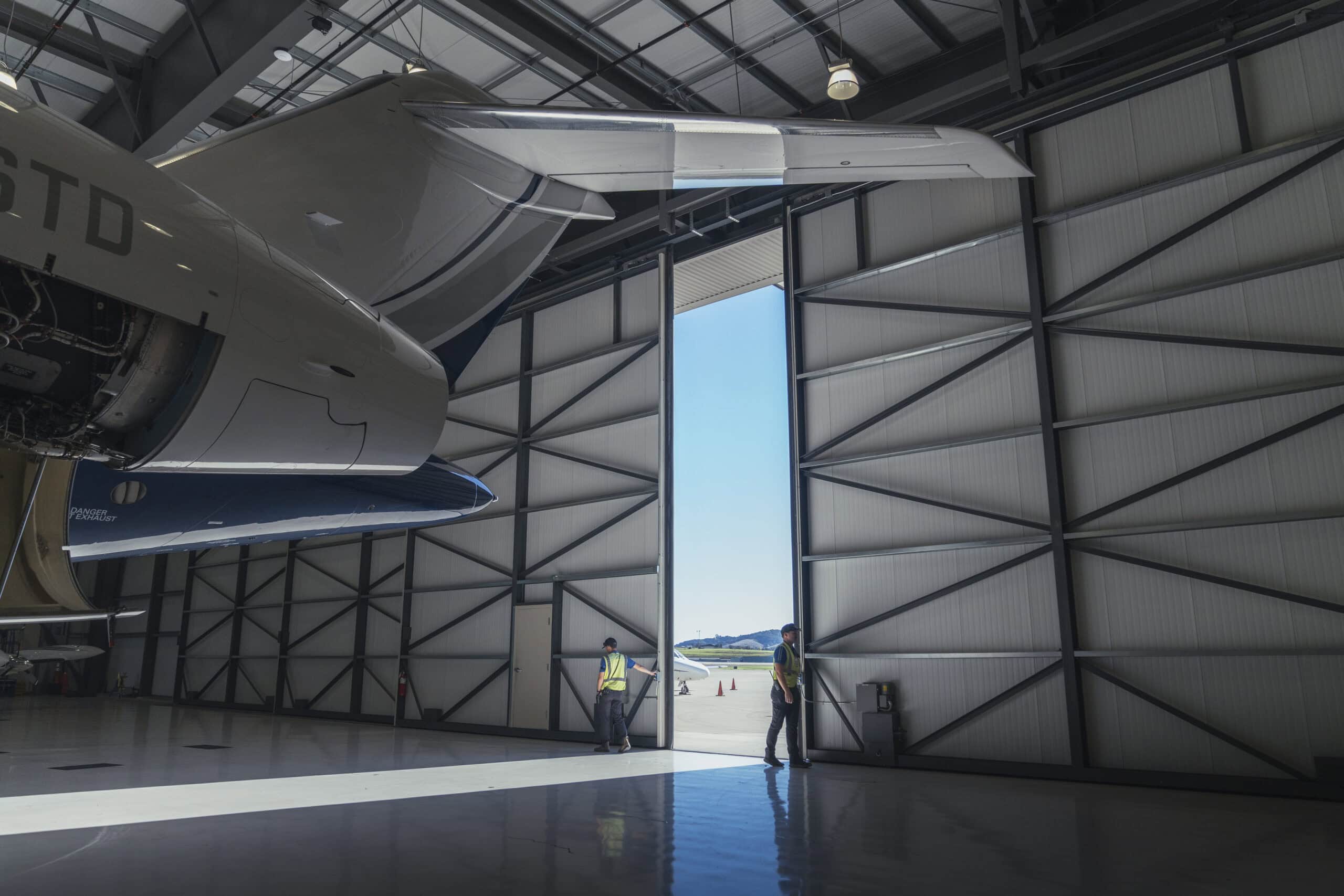 Two SLO airport workers opening doors of airport hangar with aircraft inside