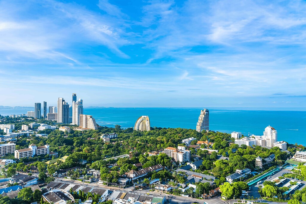 A vibrant cityscape of Pattaya with high-rise buildings, lush greenery, and the Gulf of Thailand in.