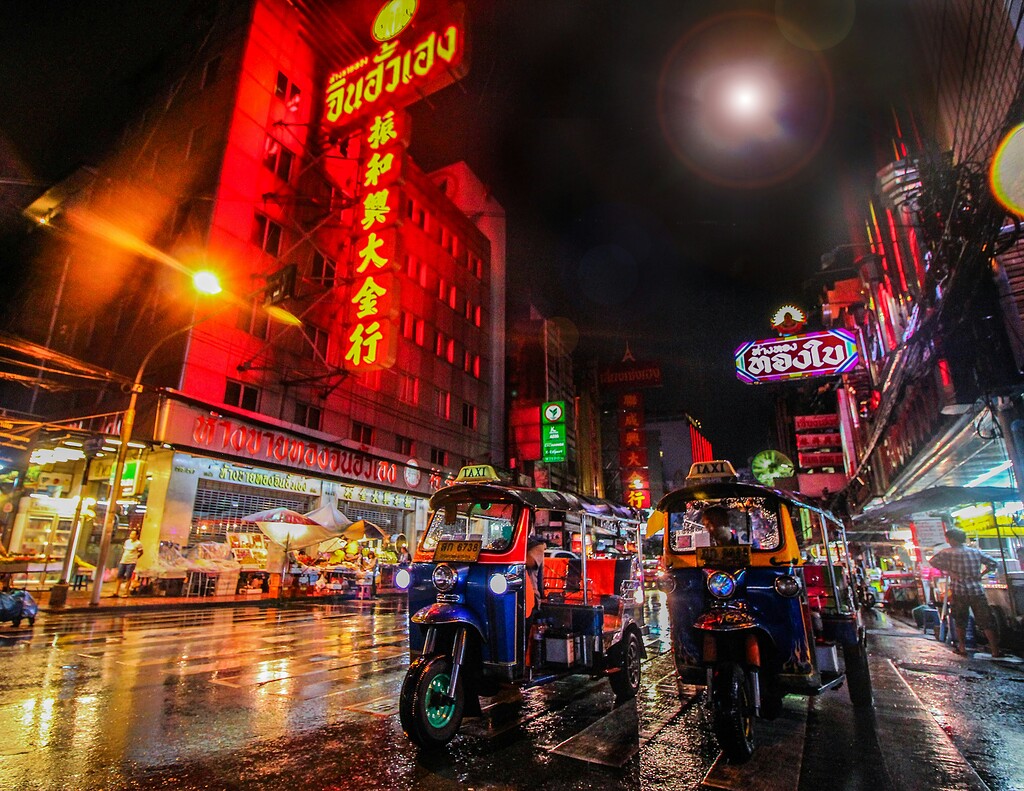 Vibrant Bangkok street at night featuring tuk-tuks, neon signs, and bustling market atmosphere.