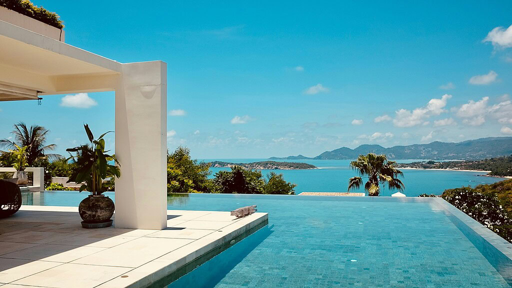 Infinity pool overlooking the ocean in Koh Samui with lush greenery and clear blue skies.