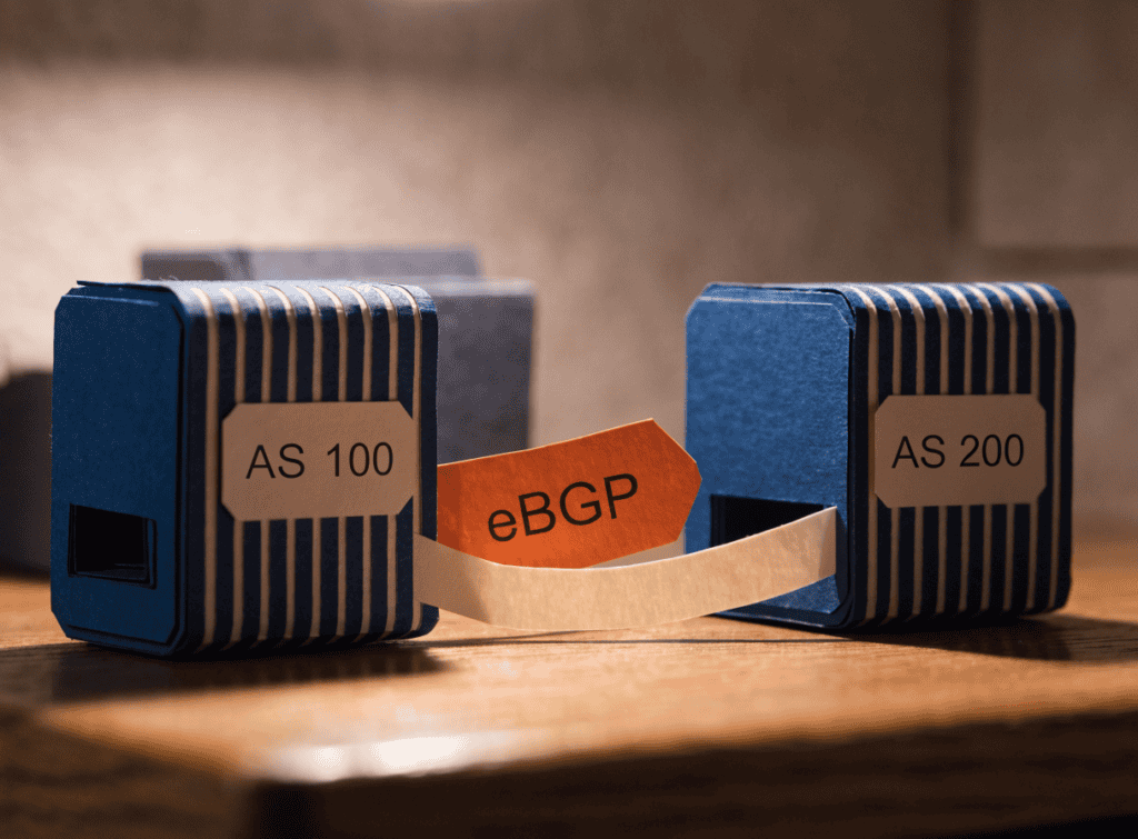 Paper-craft diagram of two routers labelled AS 100 and AS 200 connected by an eBGP peering link