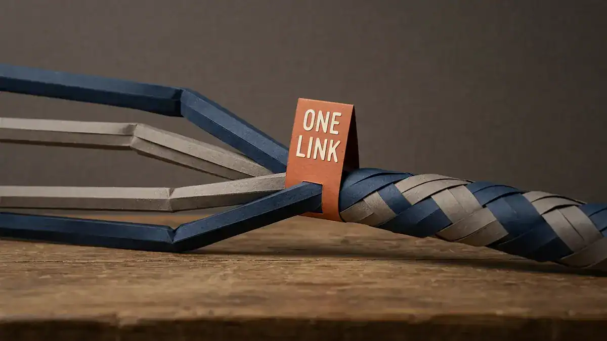 Paper-craft scene of four separate folded paper cables in navy and grey converging into a single thick woven ribbon, with a small orange paper tag reading ONE LINK where they join.
