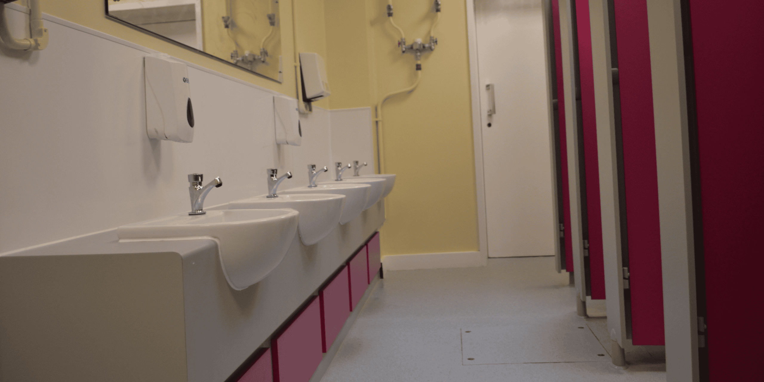 Modern washroom with row of sinks and colorful cubicle doors at Maritime Academy Trust