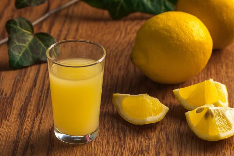 Freshly squeezed lemon juice in a glass with sliced lemons on wooden surface.