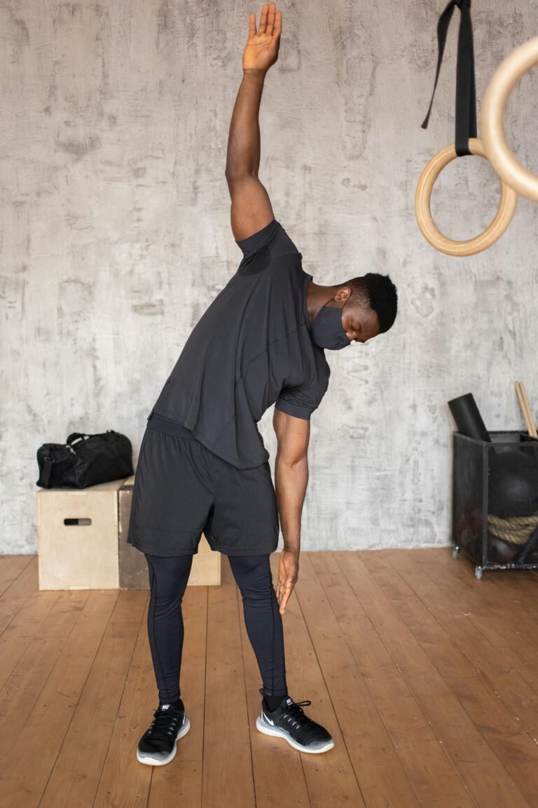 African American male athlete in sportswear doing exercises in protective mask during workout in gym