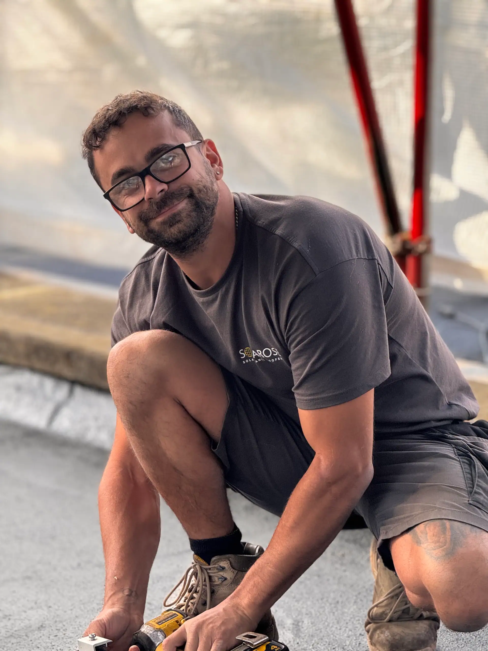 Young man with glasses and a beard installing solar panels, wearing a branded Solarose T-shirt and casual shorts.
