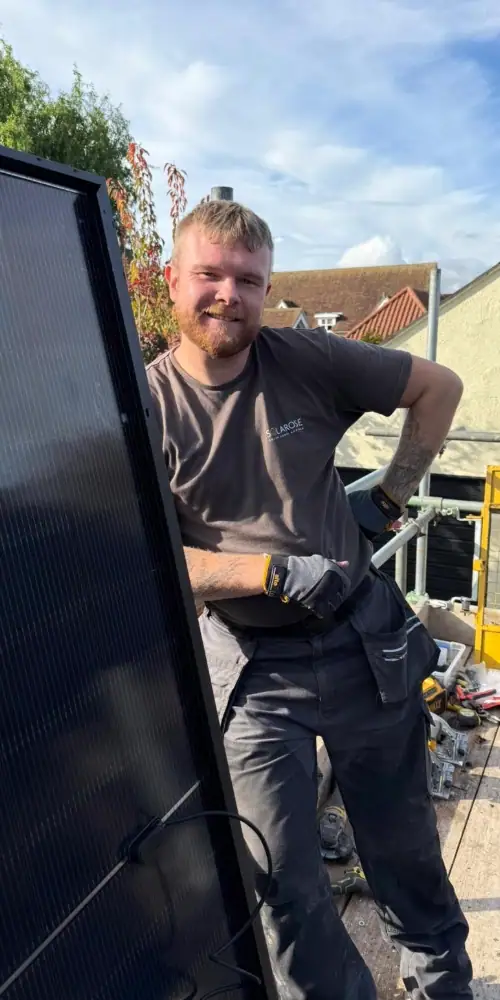 High-quality solar panel installation by a professional technician outdoors on a sunny day. The technician is smiling and standing next to solar panels in a residential setting, demonstrating expertise in sustainable energy solutions.