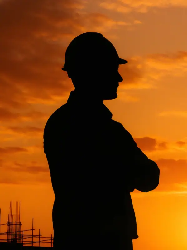 Silhouette of a construction worker wearing a helmet during sunset, symbolizing safety and professionalism in the construction and solar energy industries.