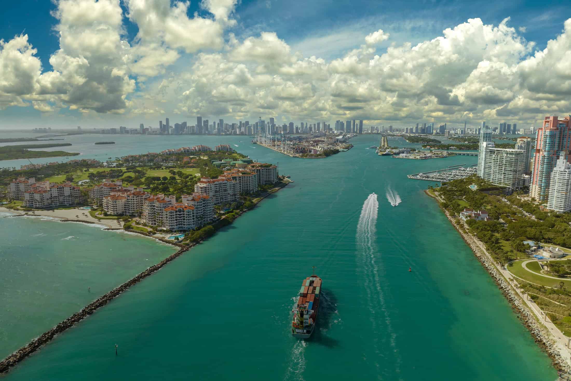 Commercial container ship entering Miami port harbor through main channel near South Beach.