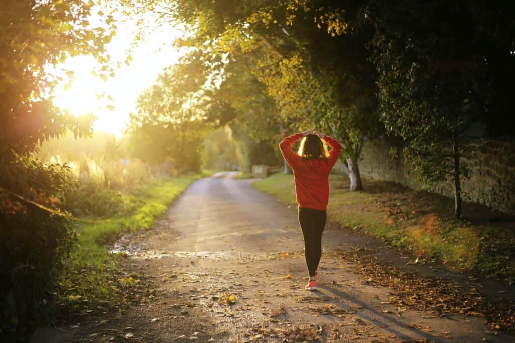 Sunlit forest trail during golden hour with a woman in athletic wear enjoying outdoor running or walking.